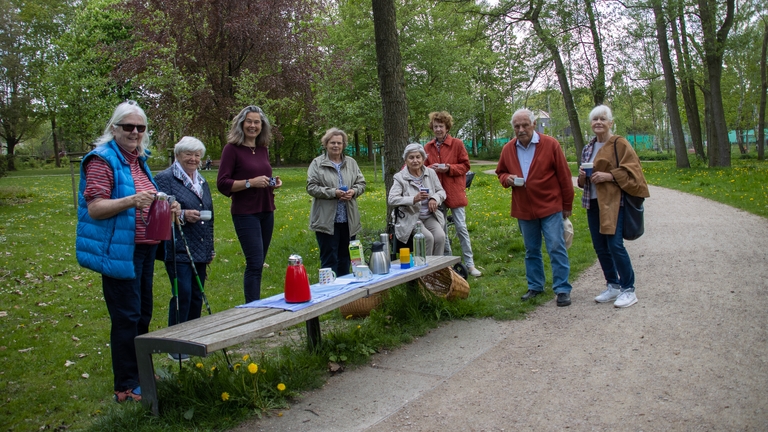 Pastorin Jürgensen mit einer Gruppe Menschen, vor sich Kannen mit Tee, Kaffee und Becher.