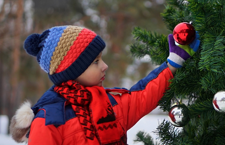Ein Kind bestaunt einen geschmückten Weihnachtsbaum im Schnee.