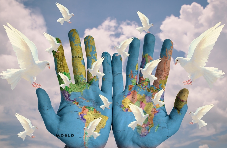 Weltkarte auf Händen umflogen von weissen Tauben, symbolisiert Frieden
