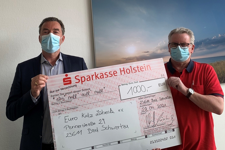 Dirk Burschberg, Leiter der Sparkasse-Holstein-Filiale in Bad Schwartau (links), und Bernd Lehmann, Gründer und Macher der Euro Kidz halten den symbolischen Scheck über 1.000 Euro.