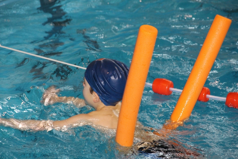 Ein Kind schwimmt in der Schwimmhalle eine Bahn mit Hilfe einer Schwimmnudel.