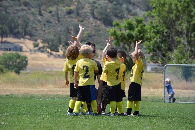 Kinder in gelb-schwarter Fußballkleidung haben sich um ihren Trainer versammelt.